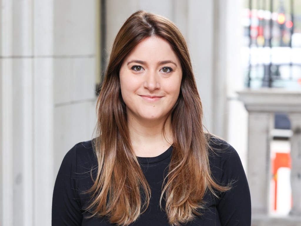 Image of Dr Rafie Cecilia, a woman with long brown/copper hair, wearing a black top, and with a slight smile. 
