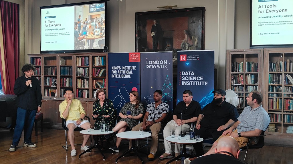 Panel discussion at the “AI Tools for Everyone: Advancing Disability Inclusion” event at the London School of Economics. Seven panellists are seated in front of banners for King’s Institute for Artificial Intelligence, London Data Week and LSE’s Data Science Institute, while a moderator stands to the left holding a microphone. Presentation screens behind them display the event title.